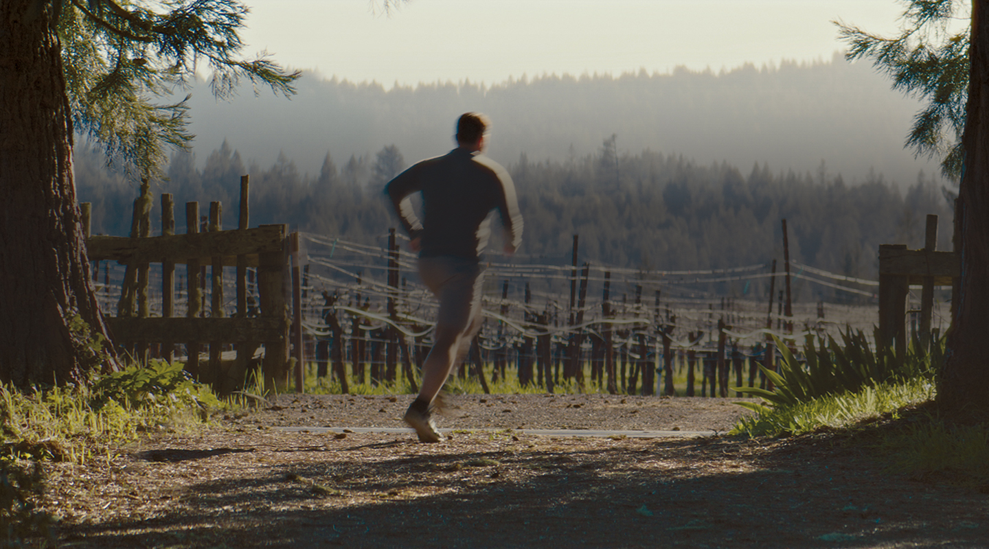 Winemaker jogging on path in vineyard with hills in background